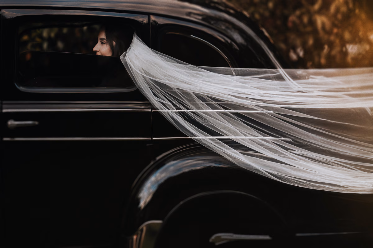 Velo de Novia sobre auto antiguo con un atardecer de fondo
